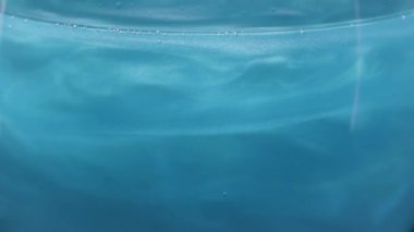Beyaz kıvılcımlı mavi sıvı kıvrılıp kıvrılır. Stok görüntüleri. Yanardöner açık mavi sıvı dokusu yavaşça hareket ediyor..
