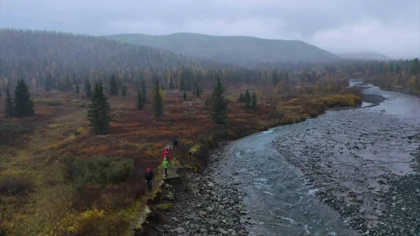 Vista aérea del grupo de personas que caminan a lo largo del río que fluye rápido. Clip. Senderistas caminando por el sendero musgoso que conduce a las montañas boscosas. —  Fotos de Stock