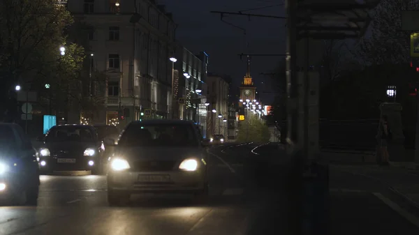 Νυχτερινή καλοκαιρινή αστική άποψη των σπάνιων αυτοκινήτων οδήγηση αργά στο δρόμο. Στικ. Νυχτερινή κίνηση στην πόλη, μετακίνηση αυτοκινήτων κατά μήκος κτιρίων και σπιτιών σε σκούρο φόντο του ουρανού. — Φωτογραφία Αρχείου