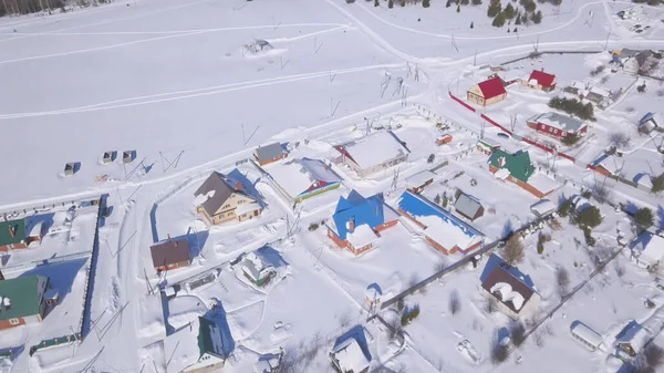 Aerial view of snow covered town and streets in winter, Switzerland countryside region. Clip. Cottages with bright roofs located near snowy white field on a sunny summer day. — Stock Photo, Image