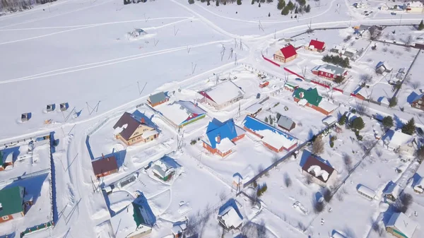 Aerial view of snow covered town and streets in winter, Switzerland countryside region. Clip. Cottages with bright roofs located near snowy white field on a sunny summer day. — Stock Photo, Image