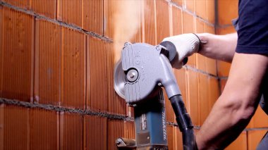 İnşaat alanındaki kırmızı blokları kesmek için öğütücü kullanan bir işçinin yan görüntüsünü kapatın. Stok görüntüleri. Usta beton bloğu tozla kesiyor..