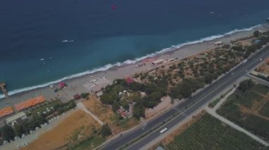 Beyaz kum, yeşil palmiye ağaçları ve mavi denizi olan tropikal bir sahil manzarası. Şarjör. Yazın güneşli bir günde, sahil boyunca uzun bir yol bulunan turistik bir tatil köyü..