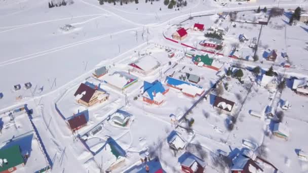 Vista aérea de la ciudad cubierta de nieve y calles en invierno, Suiza región rural. Clip. Cabañas con techos luminosos ubicados cerca del campo blanco nevado en un día soleado de verano. — Vídeo de stock