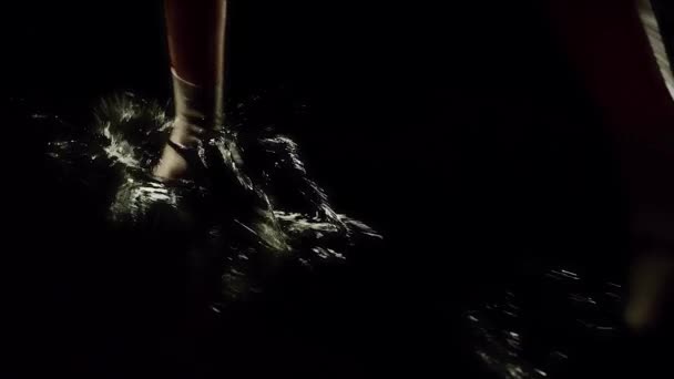 Женщина в красном платье и летних туфлях, идущая по лужному полу темной сцены. Отснятый материал. драматическая сцена театра с водой на полу и ходячая актриса во время спектакля. — стоковое видео