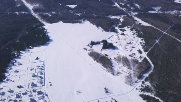 Lot nad okolicą w pochmurny zimowy dzień. Klip. Widok z lotu ptaka na zaśnieżone białe pole otoczone zalesionymi wzgórzami. — Wideo stockowe