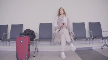 Telefonu olan kadın tren istasyonunda bekliyor. Başla. Güzel bir kadın bekleme odasında uçmayı bekliyor. Bavullu kadın tren istasyonunda telefona bakar.