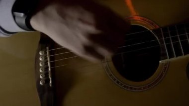 Karanlık bir odada akustik gitar çalan bir adam, müzik ve yaratıcılık kavramı. HDR. Bir arabulucuyla ritim solosu yapan erkek parmaklarının yakın görüntüsü.