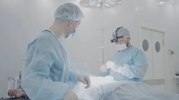 Two surgeons prepare patient for surgery. Action. Two young surgeons are preparing for operation with person under anesthesia. Surgeons begin operation — Stock Photo, Image