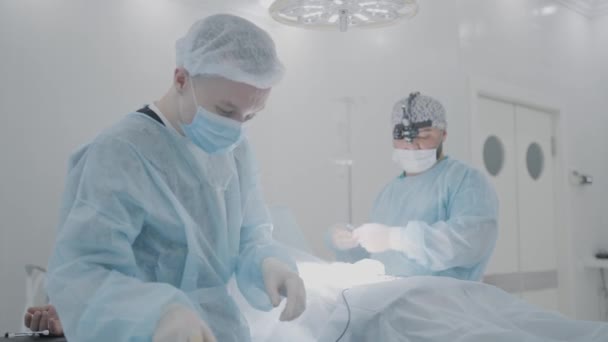 Dva chirurgové připravují pacienta na operaci. Akce. Dva mladí chirurgové se připravují na operaci s osobou v anestezii. Operace byla zahájena — Stock video