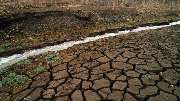 Un ruisseau qui coule dans le champ au début du printemps. Fusillade. Vue aérienne d'une étroite rivière à flexion rapide et d'un champ pierreux avec une végétation rare et croissante. — Photo
