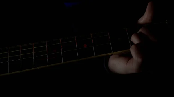 Mann spielt Akustikgitarre in einem dunklen Raum, Konzept von Musik und Kreativität. HDR. Nahaufnahme von männlichen Fingern, die mit einem Mediator ein Rhythmussolo spielen. — Stockfoto