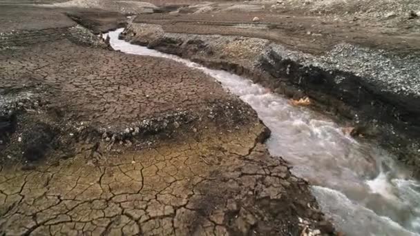 Fiume stretto che scorre e divide la terra secca. Gli hanno sparato. Paesaggio autunnale con il campo con crepe e flusso freddo veloce. — Video Stock