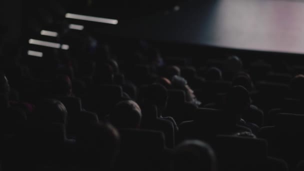 Des gens assis dans un couloir sombre et regardent un film. Vidéo. Vue arrière de personnes à la salle de cinéma regardant un film attentivement, concept de loisirs. — Video