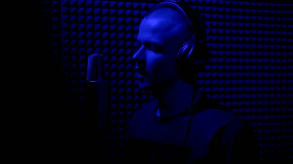 Man zingend in opnamestudio met microfoon. HDR. Zijaanzicht van een jonge mannelijke zanger die een lied opneemt in een donkere muziekstudio met blauw licht. — Stockfoto