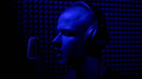 Concept van songwriting en creativiteit. HDR. Close-up zijaanzicht van een enthousiaste jonge mannelijke muzikant in oortelefoons zingen in microfoon in geluidsopname studio stand. — Stockfoto