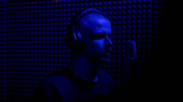 Τραγούδι στο στούντιο ηχογράφησης με μικρόφωνο. HDR. Πλευρική άποψη ενός νεαρού άνδρα τραγουδιστή που ηχογραφεί ένα τραγούδι σε ένα σκοτεινό στούντιο μουσικής με μπλε φως. — Φωτογραφία Αρχείου