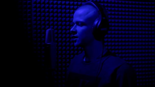Hombre cantando en estudio de grabación con micrófono. HDR. Vista lateral de un joven cantante masculino grabando una canción en un estudio de música oscura con luz azul. — Vídeos de Stock