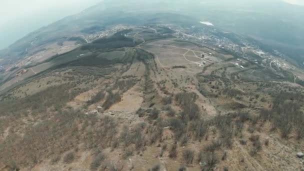 Picturesque view mountainous landscape above the village on cloudy sky background. Shot. Camera drone moving down along the dry soil slope with a green valley far in the distance. — Stock Video