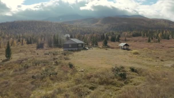 Veduta aerea di una casa in legno circondata da boschi, campi e montagne. Clip. Solitario tipica casa e le persone in piedi vicino, godendo di una natura pittoresca in campagna. — Video Stock