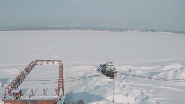 Luchtfoto van een oude pier en een afgemeerd roestig schip op een besneeuwde oever. Een knip. Winterlandschap van een verlaten pier en een schip op de achtergrond van kranen en bouwplaatsen. — Stockvideo