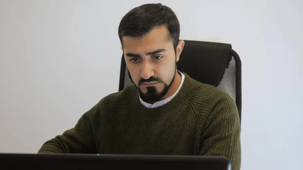 El hombre está trabajando intensamente en la computadora portátil en la oficina. HDR. Hombre guapo está trabajando en el portátil en suéter. Freelancer o escritor que trabaja en laptop — Foto de Stock