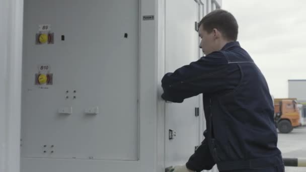 Vista lateral de un trabajador abre la puerta de una cabina de metal para el almacenamiento de equipos mecánicos y tomar un cable. Escena. Detalles de los trabajos del centro de reparación, antecedentes industriales. — Vídeos de Stock