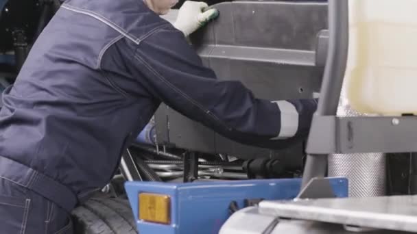 Inspector profesional en el servicio de reparación quitando la cubierta del motor de un camión nuevo. Escena. Mantenimiento técnico de una máquina en el taller. — Vídeos de Stock