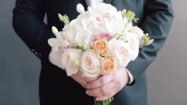 Damat düğün buketini yakından tutuyor. Video kaydı. Elinde bir buket düğün çiçeği olan damat ayakta duruyor. Damat bir buket tutuyor.