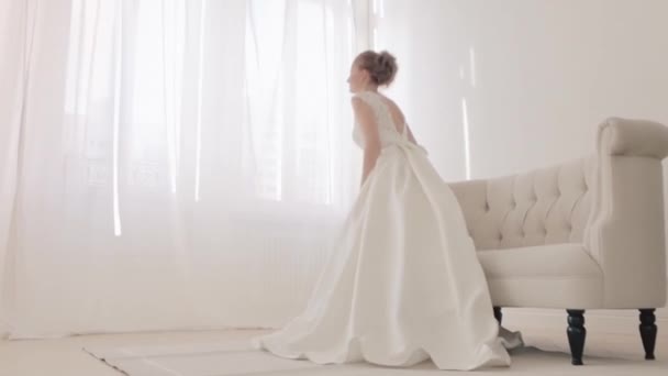 ループと白い優雅結婚式のドレスで花嫁のバック。ビデオだ。全長。結婚式。美しい花嫁室内の花束と大きな窓に対するフルライトバック側の景色 — ストック動画