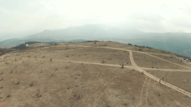 Aerial panoramic view of a scenic hilly dry valley surrounded by Canadian mountain landscape. Shot. Concept of travelling, flying above narrow paths on fields with foggy mountains on the background. — Stock Video