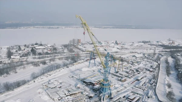 Luchtfoto van een industriezone op een winterdag en een brede met ijs bedekte rivier op de achtergrond. Een knip. Bouwplaats met kranen en besneeuwde straten. — Stockfoto