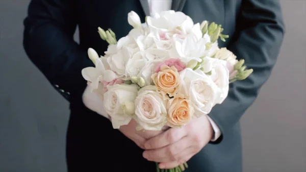 Damat düğün buketini yakından tutuyor. Video kaydı. Elinde bir buket düğün çiçeği olan damat ayakta duruyor. Damat bir buket tutuyor. — Stok fotoğraf