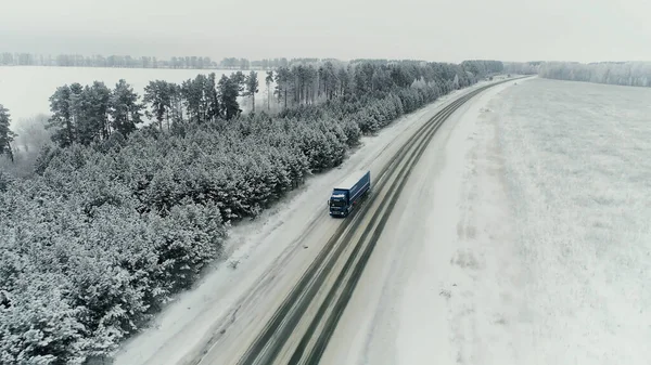 Luchtfoto van een vrachtwagen die op een heldere winterdag over een rijweg langs een spoorweg rijdt. Vrachtwagens vervoeren containers door de ruige besneeuwde woestijn in Utah. — Stockfoto