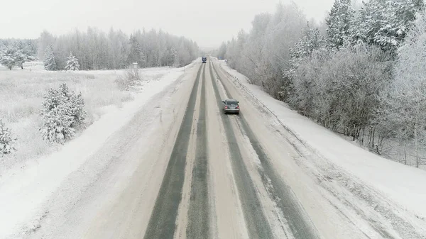 Vrachtwagen rijden langs de weg door het winterbos. Plaats delict. Uitzicht vanuit de lucht op autorijden in de winter, weg omgeven door prachtig bos bedekt met sneeuw — Stockfoto