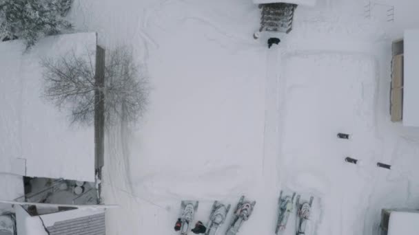 Flygfoto över en snöig innergård med små hus och parkerade snöskotrar och bilar. Klipp. Tak av byggnader täckta av snö och en gående man. — Stockvideo
