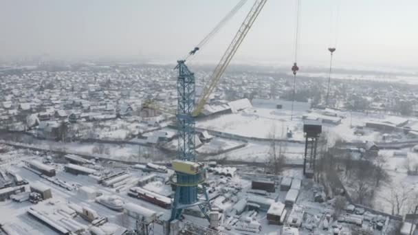 Widok z lotu ptaka na plac budowy miasta z dźwigiem w śnieżny zimowy dzień. Klip. Przemysłowa strefa dużego miasta i dachy budynków pokryte białym śniegiem. — Wideo stockowe