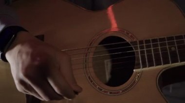 Gitar çalan adamın yakın çekimi. HDR. Adam evde basit akustik gitar çalıyor. Genç adam yarı karanlıkta gitar çalar.
