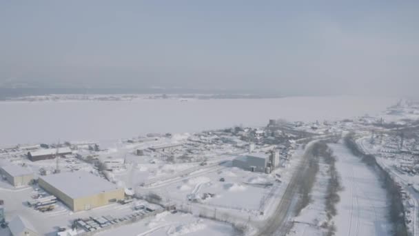 Kış şehrinin varoş, köy ya da sanayi bölgesi. Şarjör. Karla kaplı bir kasabanın hava manzarası ve geniş bir nehir.. — Stok video