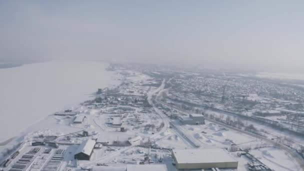 Un barrio, pueblo o barrio industrial de una ciudad invernal. Clip. Vista aérea de un pueblo situado junto a la nieve y el hielo cubierto de ancho río. — Vídeo de stock