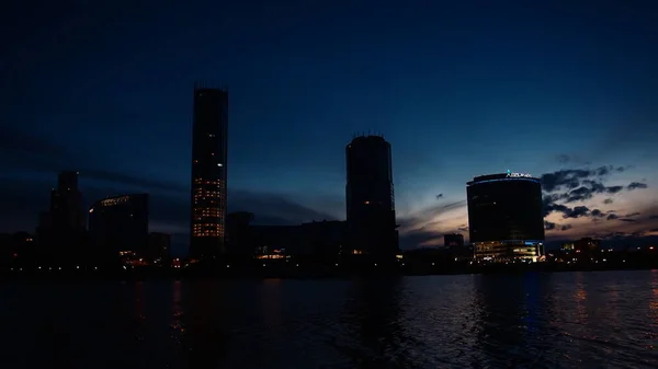 Hermoso paisaje con un río que fluye y cielo azul oscureciendo al atardecer con una ciudad al fondo. Vídeo. Efecto Timelapse de una ciudad con rascacielos situados a lo largo del río. — Foto de Stock