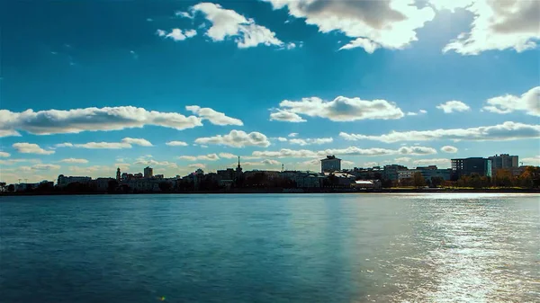 Hermoso paisaje con un río que fluye y el cielo azul nublado reflejado en la superficie del agua con una ciudad en el fondo. Vídeo. Efecto Timelapse de una ciudad situada a lo largo del río. — Foto de Stock