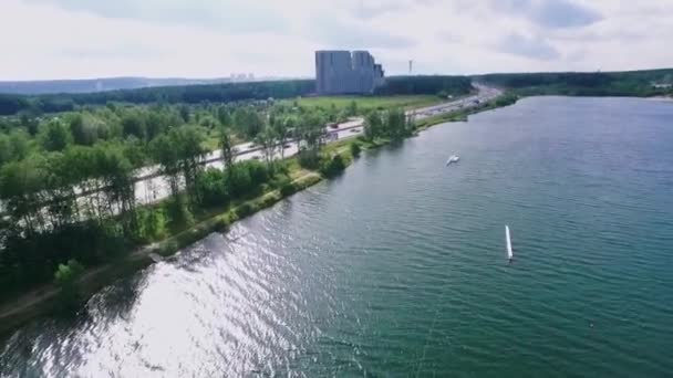 Luchtfoto van de groene natuur in de buurt van de rivier gelegen buiten de stad. Een video. Brede rustige rivier en een weg met rijdende auto 's op een zonnige zomerdag. — Stockvideo