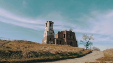 Mavi bulutlu gökyüzü arka planında antik bir taş kilise binası. Video kaydı. Kırmızı tuğlalı eski bir bina, sonbahar ağaçları ve bir çayır manzarası..