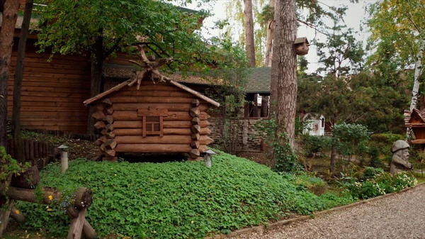 Detalhes de um parque de verão com casas tradicionais de madeira de conto de fadas russas cercadas por gramado verde e árvores. Vídeo. Uma cabana em pernas de frango ou cabana Baba Yaga No folclore eslavo. — Fotografia de Stock