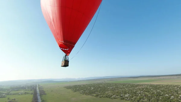 青い澄んだ空を飛ぶハート型の赤い熱気球。撃たれた。ロマンチックなデート、旅行、冒険の概念. — ストック写真