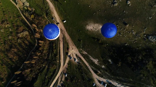 Vue aérienne de deux montgolfières bleues volant au-dessus des routes rurales et des arbres et champs verts. Fusillade. Voler dans le ciel au-dessus de la nature verte. — Photo