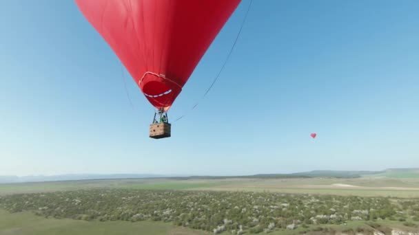 Globo de aire caliente rojo de forma de corazón volando en el cielo azul claro. Le dispararon. Concepto de una cita romántica, viaje y aventura. — Vídeos de Stock