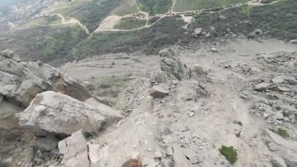 Fliegen am Hang des felsigen Berges entlang in Richtung des grünen Tals. Schuss. Luftaufnahme von steinigen Berghängen und schmalen Wegen in der Landschaft. — Stockvideo