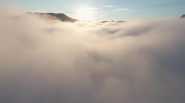 Dağ zirvelerinin arka planında kalın bulutlar. Vuruldu. Mavi gökyüzü ve güneşin arka planında yüksek dağların tepeleri olan güzel bulutlu bir manzara. Dağların üzerindeki bulutlarla nefes kesici manzara